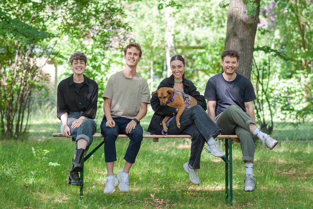Vier junge Menschen sitzen nebeneinander auf einer Bank und lächeln.
