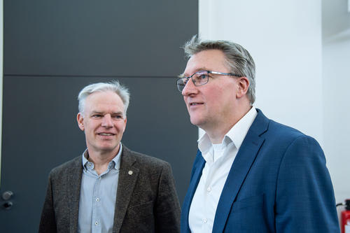 Rainer Haag (links) und Sebastian Hasenstab-Riedel (rechts) Zwei Männer in Businesskleidung unterhalten sich in einem modernen Innenraum. Der Mann links trägt ein graues Sakko, der rechte ein blaues. Beide wirken konzentriert und freundlich.